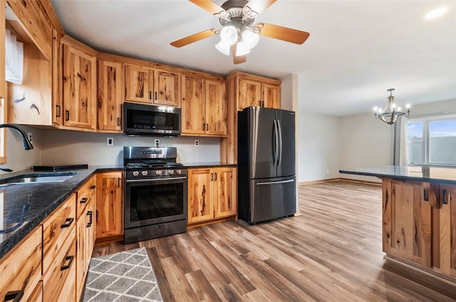 kitchen featuring stainless steel appliances, a sink, wood finished floors, baseboards, and ceiling fan with notable chandelier