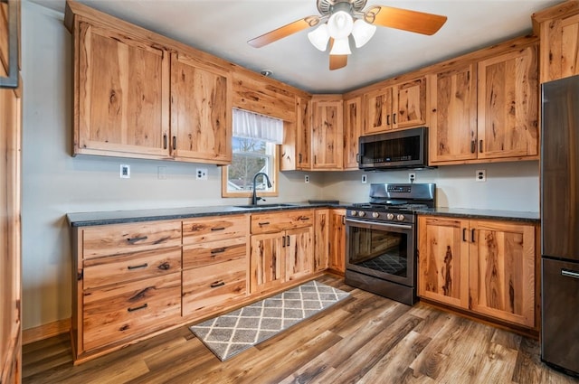 kitchen featuring refrigerator, a sink, wood finished floors, stainless steel range with gas cooktop, and dark countertops