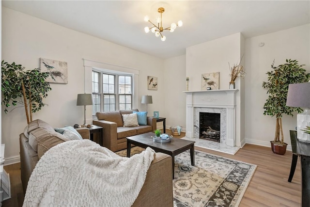 living area with light wood-style flooring, a chandelier, baseboards, and a high end fireplace