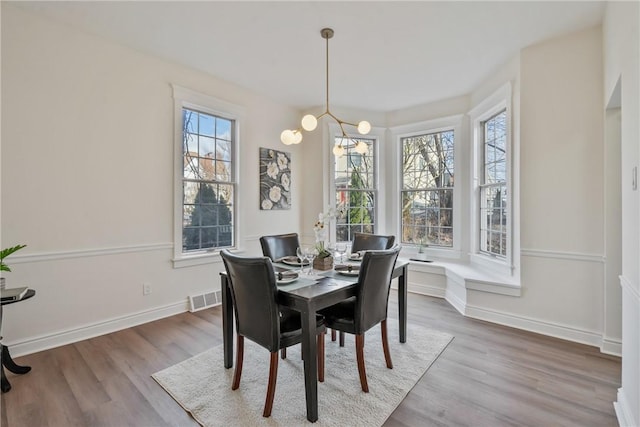 dining room featuring baseboards, a notable chandelier, visible vents, and wood finished floors