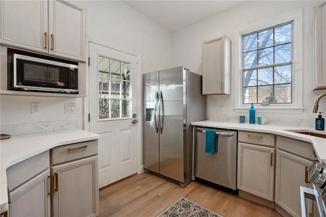 kitchen with light wood-style flooring, appliances with stainless steel finishes, gray cabinets, light countertops, and a sink