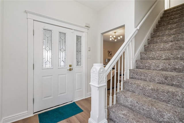 entrance foyer with wood finished floors, an inviting chandelier, and stairs