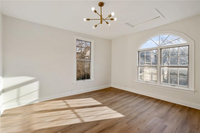 empty room with a chandelier, wood finished floors, and baseboards