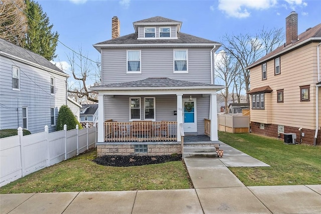 american foursquare style home featuring a chimney, a porch, a front yard, central AC, and fence