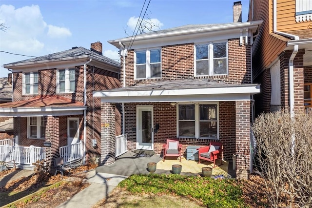 view of front of home with a patio, brick siding, a chimney, and a porch