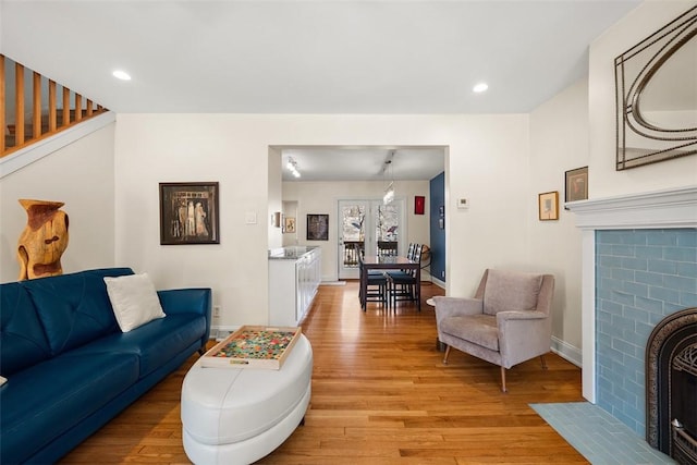 living area with a tile fireplace, light wood-style flooring, recessed lighting, baseboards, and stairs