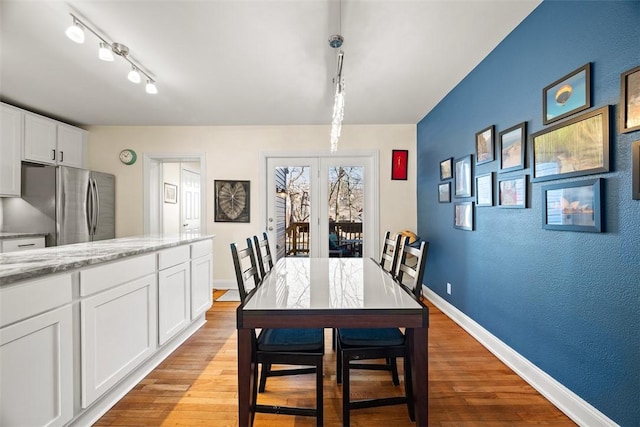 dining space with track lighting, light wood-style flooring, and baseboards