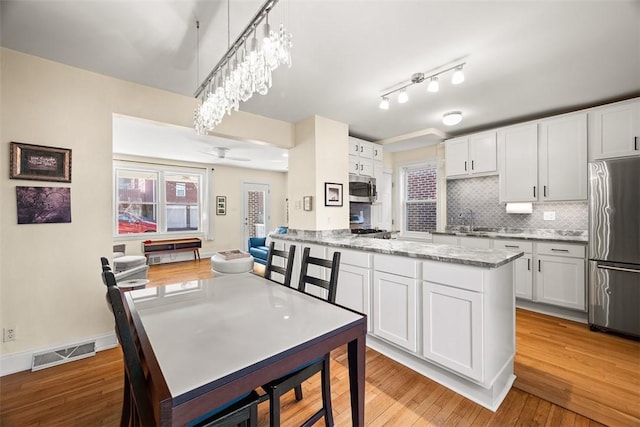 kitchen with visible vents, decorative backsplash, light wood-style flooring, appliances with stainless steel finishes, and white cabinetry