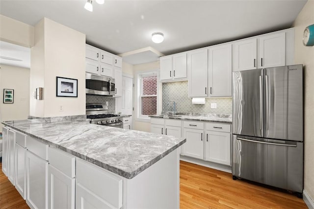 kitchen featuring light stone counters, stainless steel appliances, light wood-style floors, white cabinets, and a peninsula