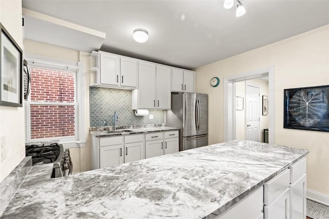 kitchen with light stone counters, appliances with stainless steel finishes, backsplash, and a sink