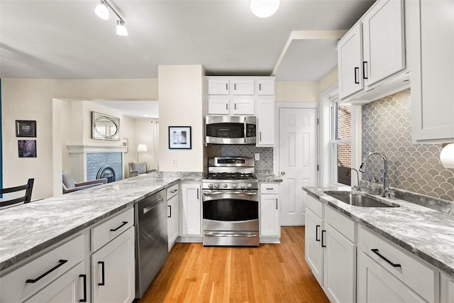 kitchen featuring appliances with stainless steel finishes, a sink, light stone counters, and light wood-style floors