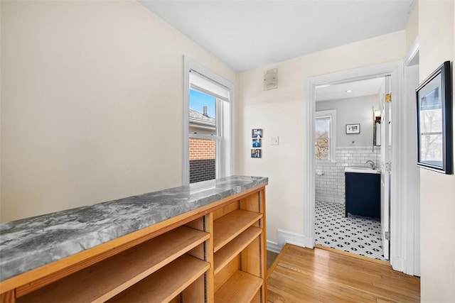 bar featuring a healthy amount of sunlight, light wood finished floors, tile walls, and a sink