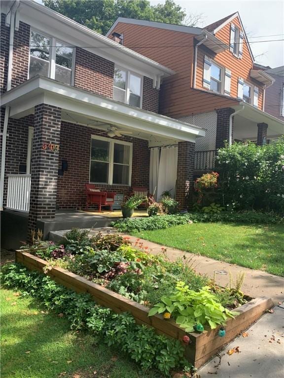 view of front facade featuring covered porch, a garden, a front lawn, and brick siding