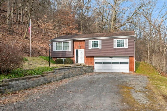 raised ranch with a garage, driveway, and brick siding