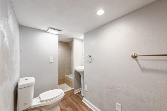 full bathroom featuring baseboards, toilet, wood finished floors, and a tile shower