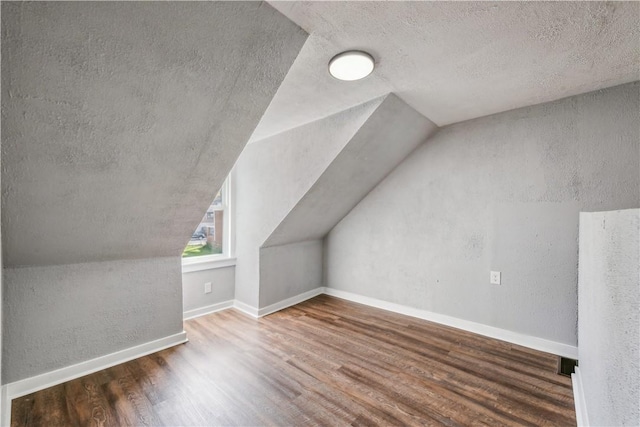 additional living space featuring lofted ceiling, wood finished floors, baseboards, and a textured ceiling