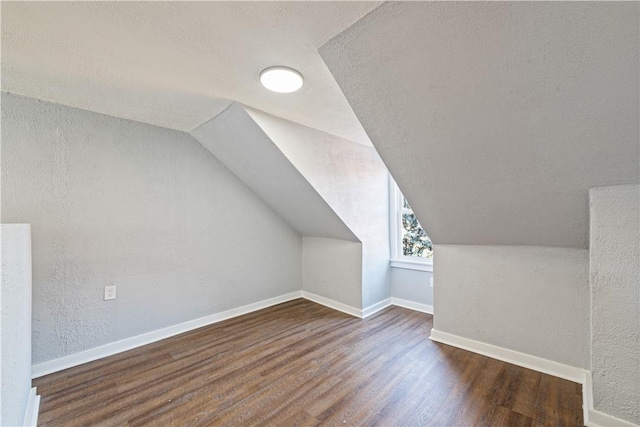 bonus room featuring lofted ceiling, a textured ceiling, wood finished floors, baseboards, and a textured wall