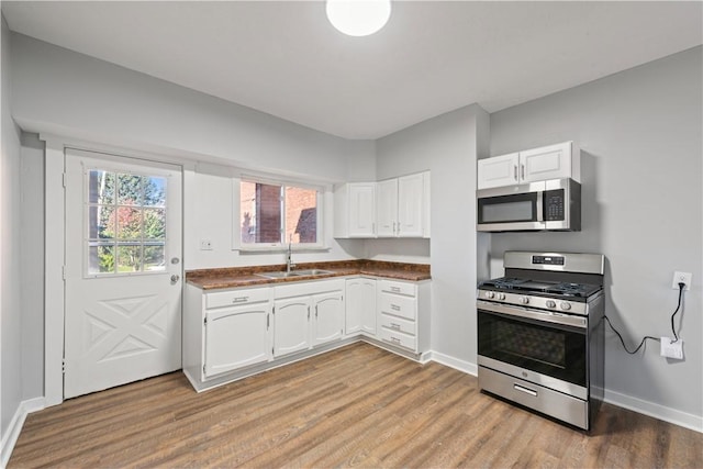 kitchen featuring a sink, stainless steel appliances, white cabinetry, dark countertops, and light wood-type flooring