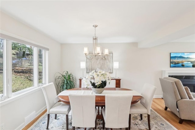 dining space featuring baseboards, light wood-type flooring, a high end fireplace, and an inviting chandelier