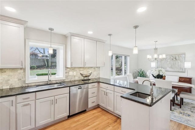 kitchen featuring dishwasher, dark stone countertops, a sink, and light wood-style flooring