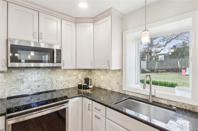 kitchen featuring dark stone counters, appliances with stainless steel finishes, hanging light fixtures, a sink, and backsplash