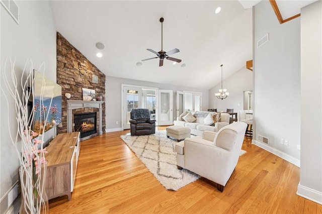 living area with light wood-type flooring, high vaulted ceiling, visible vents, and a stone fireplace