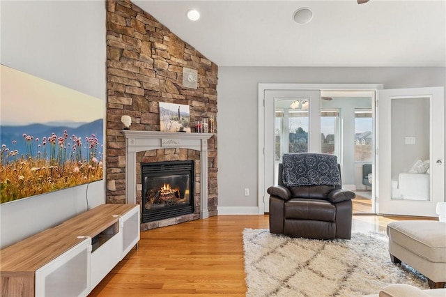 living room featuring light wood finished floors, baseboards, vaulted ceiling, and a stone fireplace