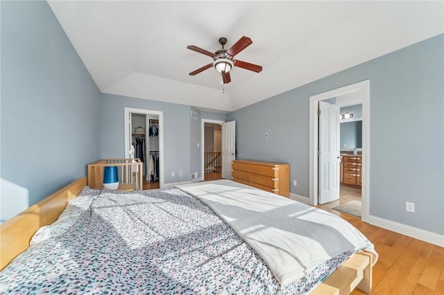 bedroom featuring wood finished floors, baseboards, a closet, a tray ceiling, and a walk in closet