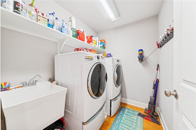 washroom with light wood-style flooring, a sink, laundry area, independent washer and dryer, and baseboards