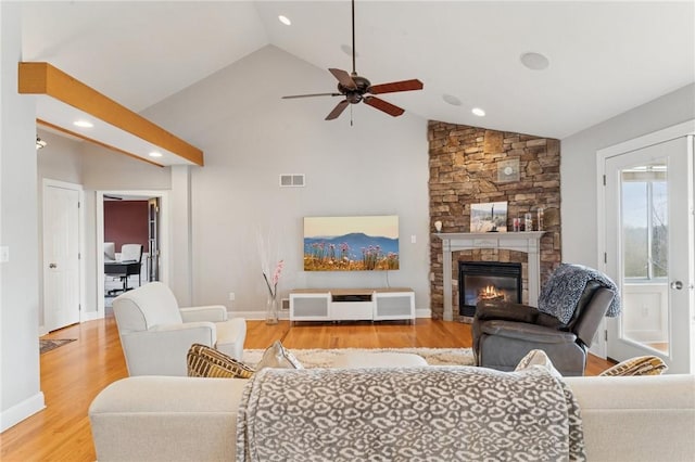 living area featuring baseboards, visible vents, a stone fireplace, light wood-type flooring, and high vaulted ceiling