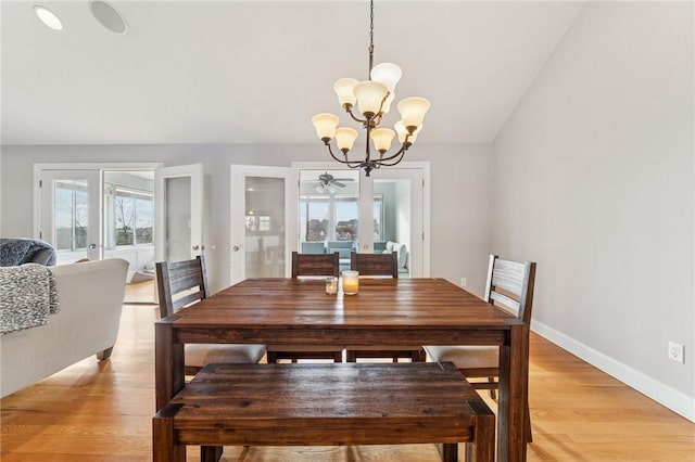 dining area with light wood-type flooring, vaulted ceiling, baseboards, and an inviting chandelier