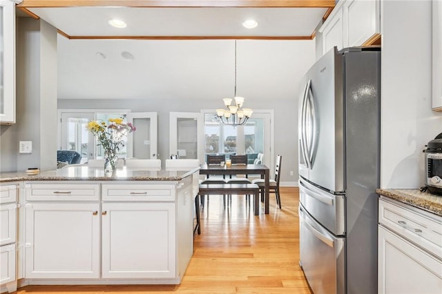 kitchen with a chandelier, white cabinetry, light wood-type flooring, freestanding refrigerator, and light stone countertops