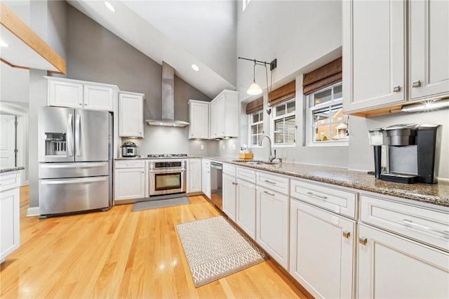 kitchen featuring stainless steel appliances, light wood-type flooring, wall chimney range hood, white cabinetry, and a sink