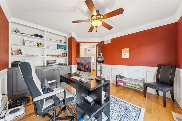 home office with a wainscoted wall, wood finished floors, visible vents, and a ceiling fan