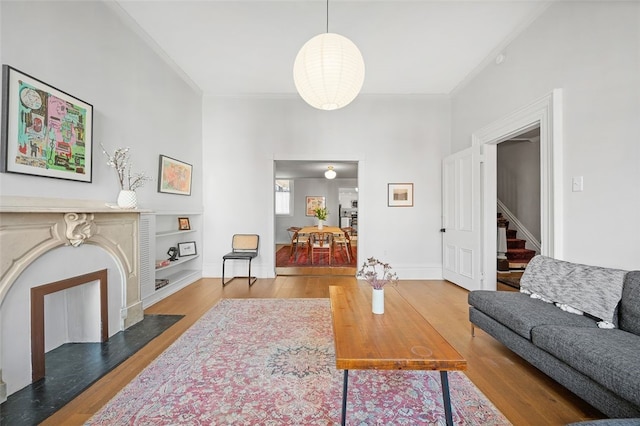 living room with crown molding, a fireplace with flush hearth, wood finished floors, baseboards, and stairs