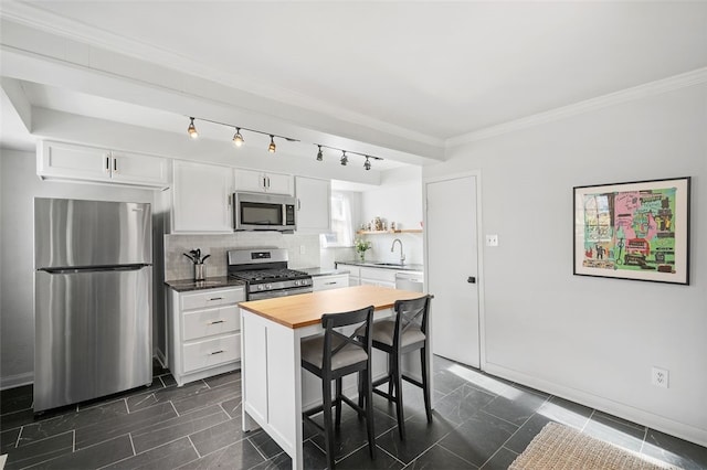 kitchen featuring stainless steel appliances, wooden counters, decorative backsplash, ornamental molding, and white cabinetry