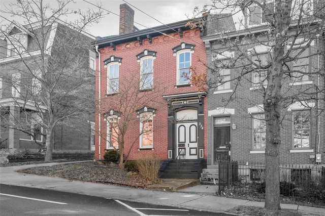 view of front of house featuring entry steps, brick siding, and a chimney