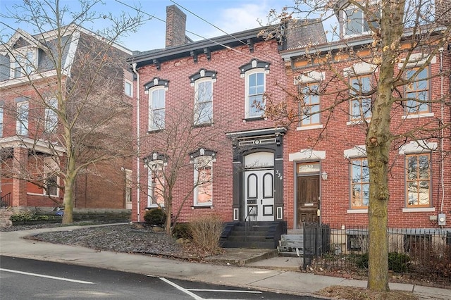 view of front of property with a chimney, fence, and brick siding