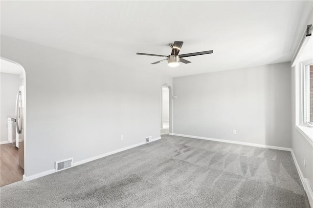 carpeted spare room with visible vents, arched walkways, ceiling fan, and baseboards