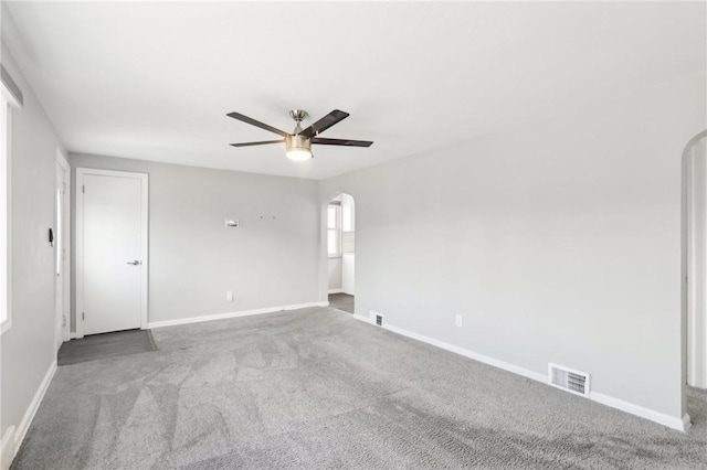 carpeted empty room with arched walkways, visible vents, ceiling fan, and baseboards