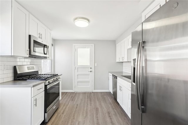 kitchen featuring light wood-style flooring, stainless steel appliances, white cabinetry, baseboards, and tasteful backsplash