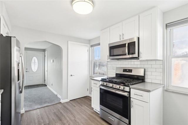 kitchen with arched walkways, a wealth of natural light, backsplash, appliances with stainless steel finishes, and white cabinetry