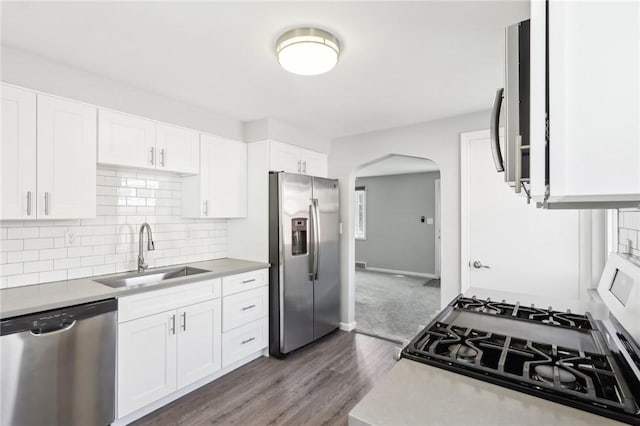 kitchen featuring arched walkways, tasteful backsplash, light countertops, appliances with stainless steel finishes, and a sink