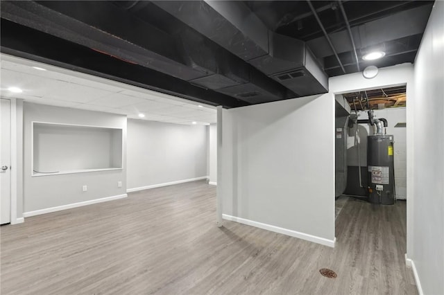 finished basement with visible vents, water heater, baseboards, and wood finished floors