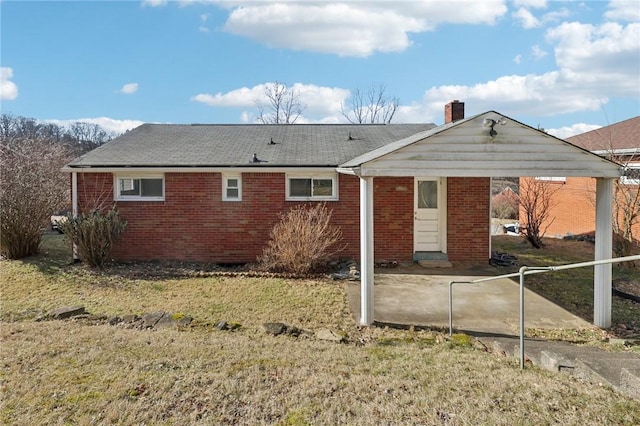 back of house featuring brick siding, a lawn, and a chimney