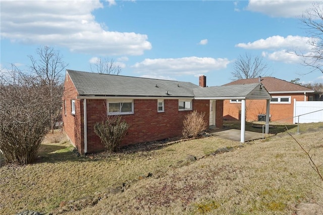 back of house featuring a lawn, a chimney, fence, a patio area, and brick siding