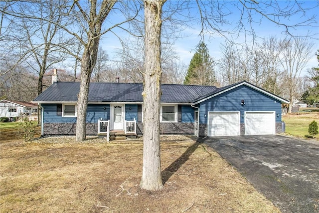 single story home with a chimney, an attached garage, metal roof, stone siding, and driveway