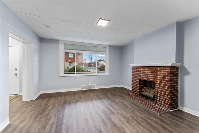 unfurnished living room with a brick fireplace, wood finished floors, visible vents, and baseboards