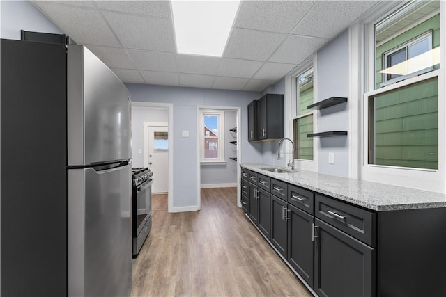 kitchen with range with gas stovetop, open shelves, freestanding refrigerator, a sink, and light wood-type flooring