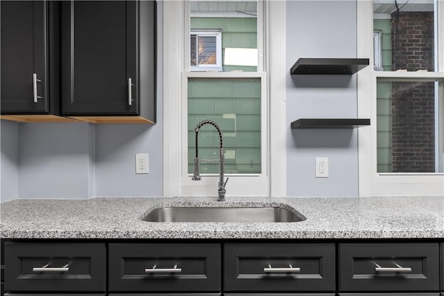 kitchen featuring dark cabinets, light stone countertops, and a sink